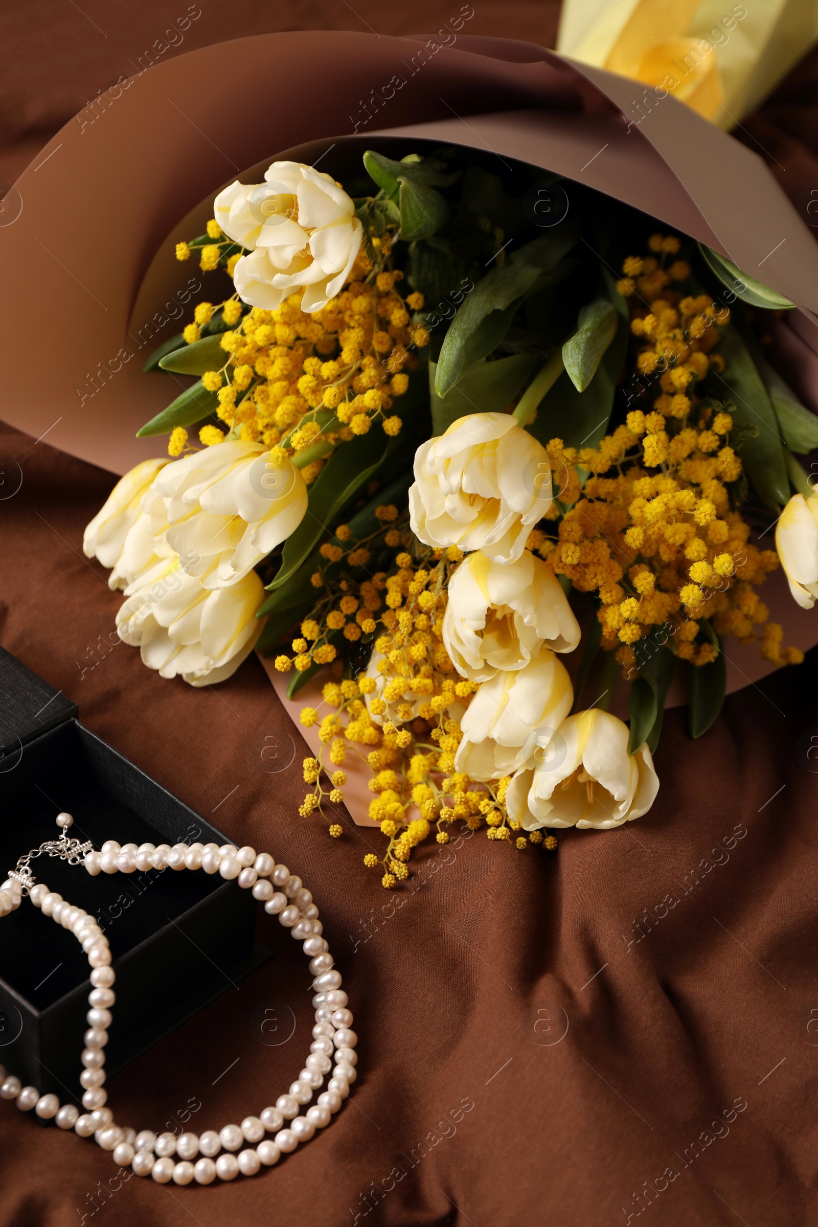 Photo of Bouquet of beautiful spring flowers and necklace on brown fabric, above view