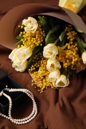 Bouquet of beautiful spring flowers and necklace on brown fabric, above view