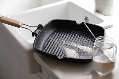 Photo of Dirty grill pan and jar with baking soda on countertop near sink in kitchen