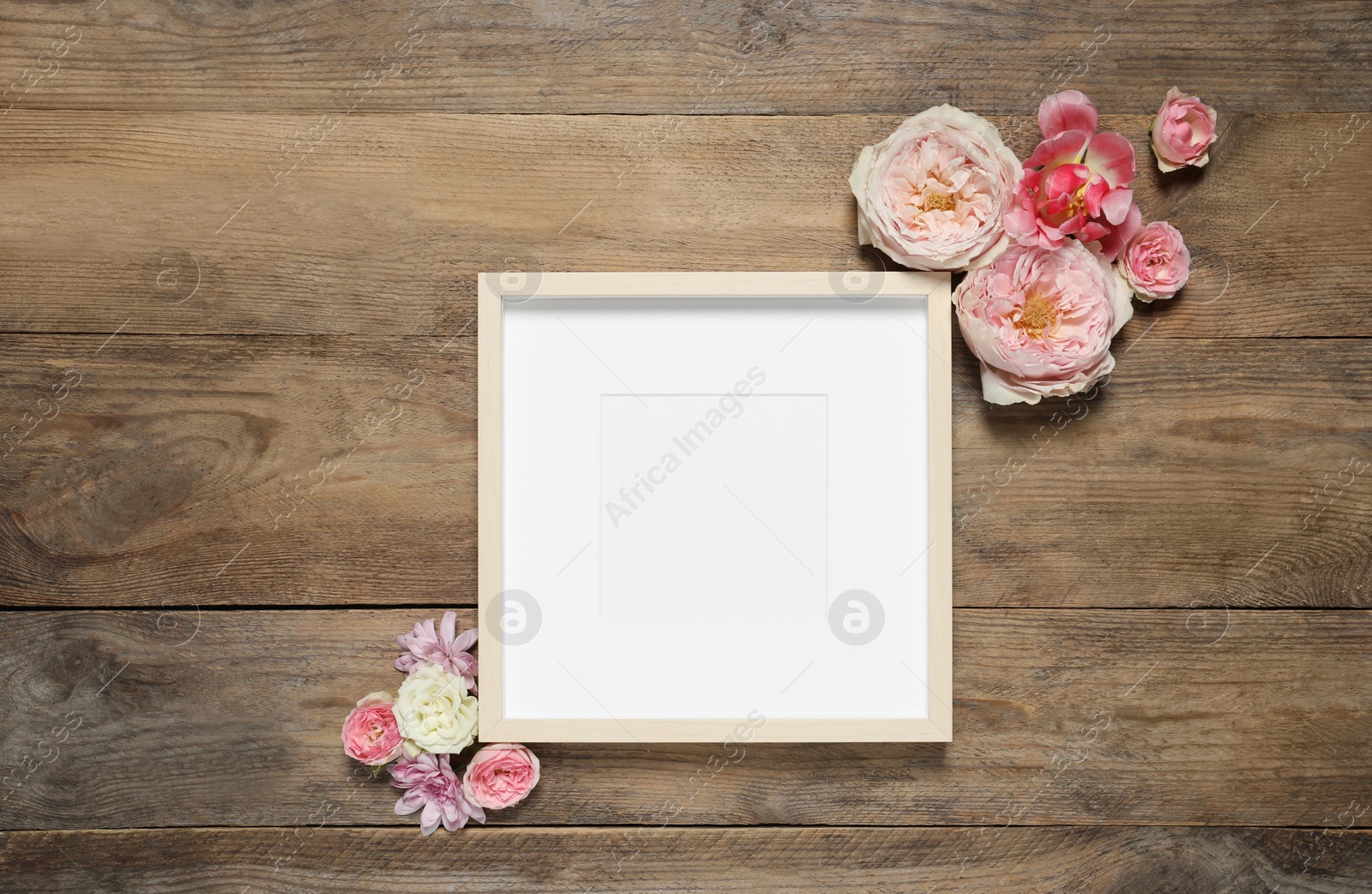 Photo of Empty photo frame and beautiful flowers on wooden table, flat lay. Space for design