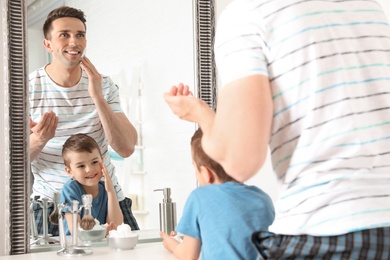 Dad shaving and little son imitating him in bathroom