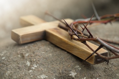 Photo of Crown of thorns and wooden cross on stone, closeup. Easter attributes