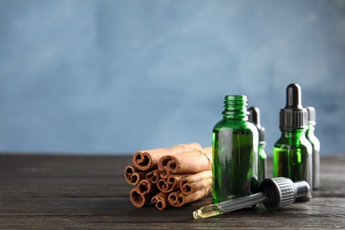 Photo of Bottles with essential oil and cinnamon sticks on wooden table against blue background