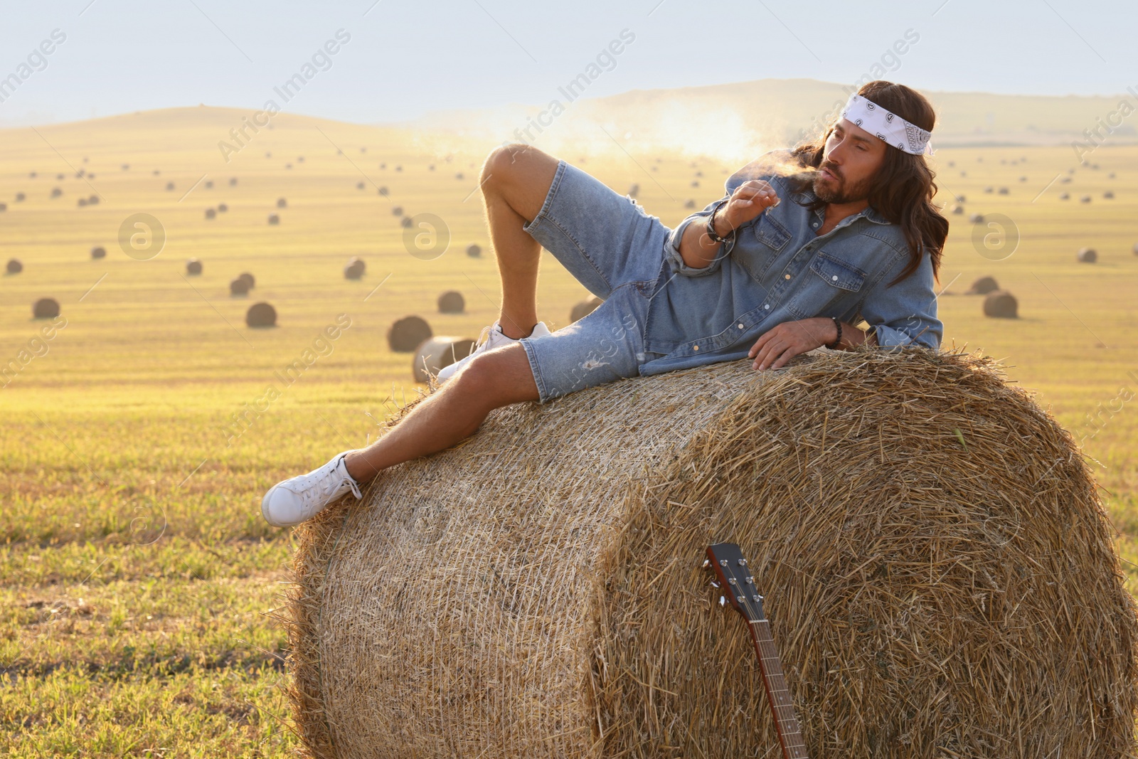 Photo of Hippie man smoking joint on hay bale in field