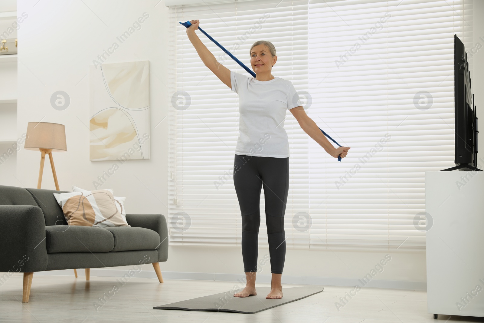 Photo of Senior woman doing exercise with fitness elastic band on mat at home