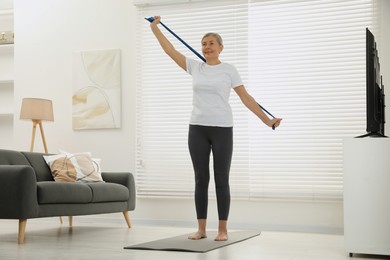 Senior woman doing exercise with fitness elastic band on mat at home