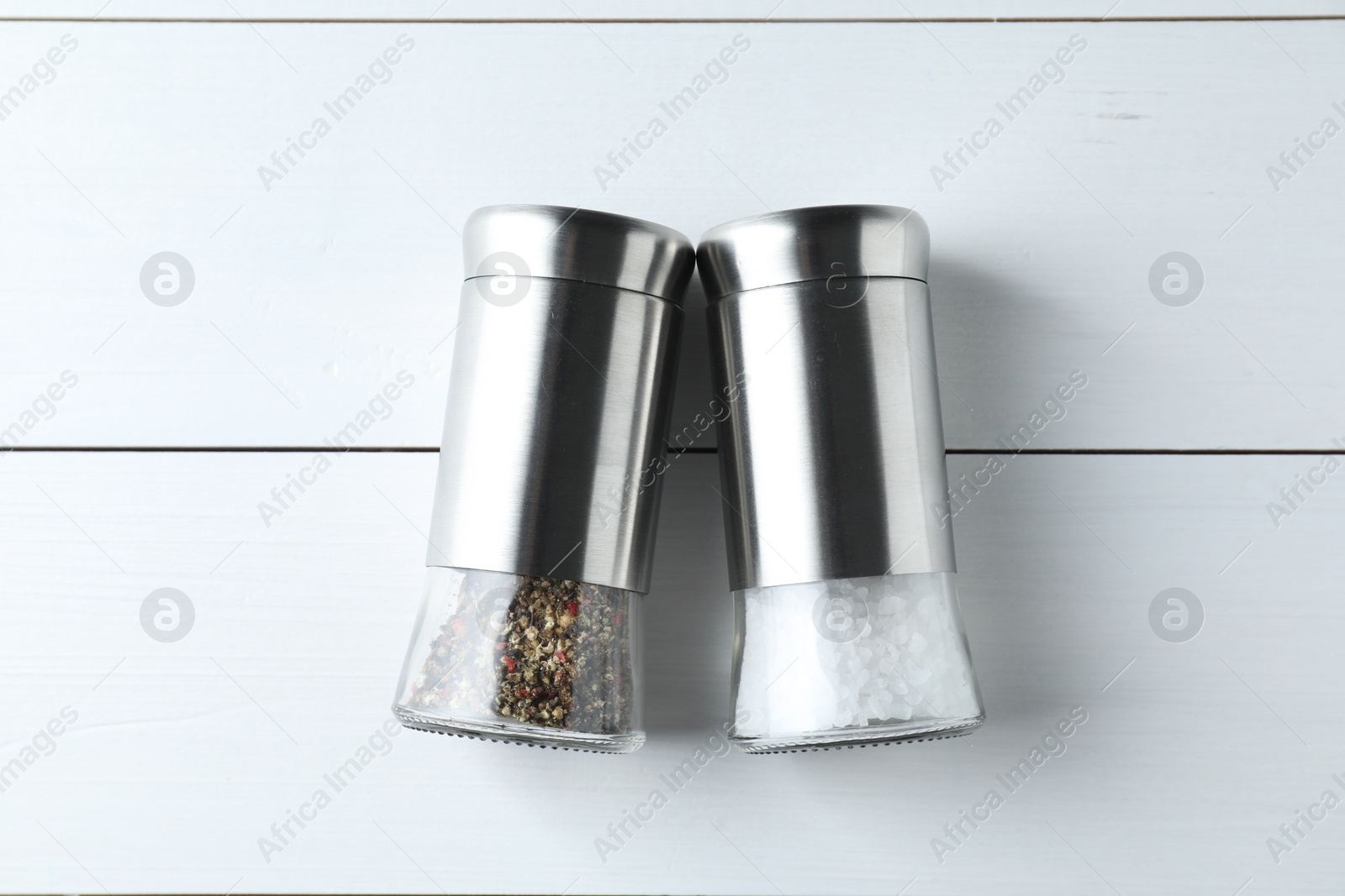 Photo of Salt and pepper shakers on white wooden table, flat lay