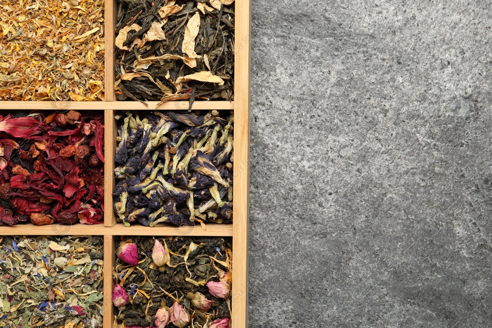 Photo of Different dry herbal teas in wooden box on grey table, top view. Space for text