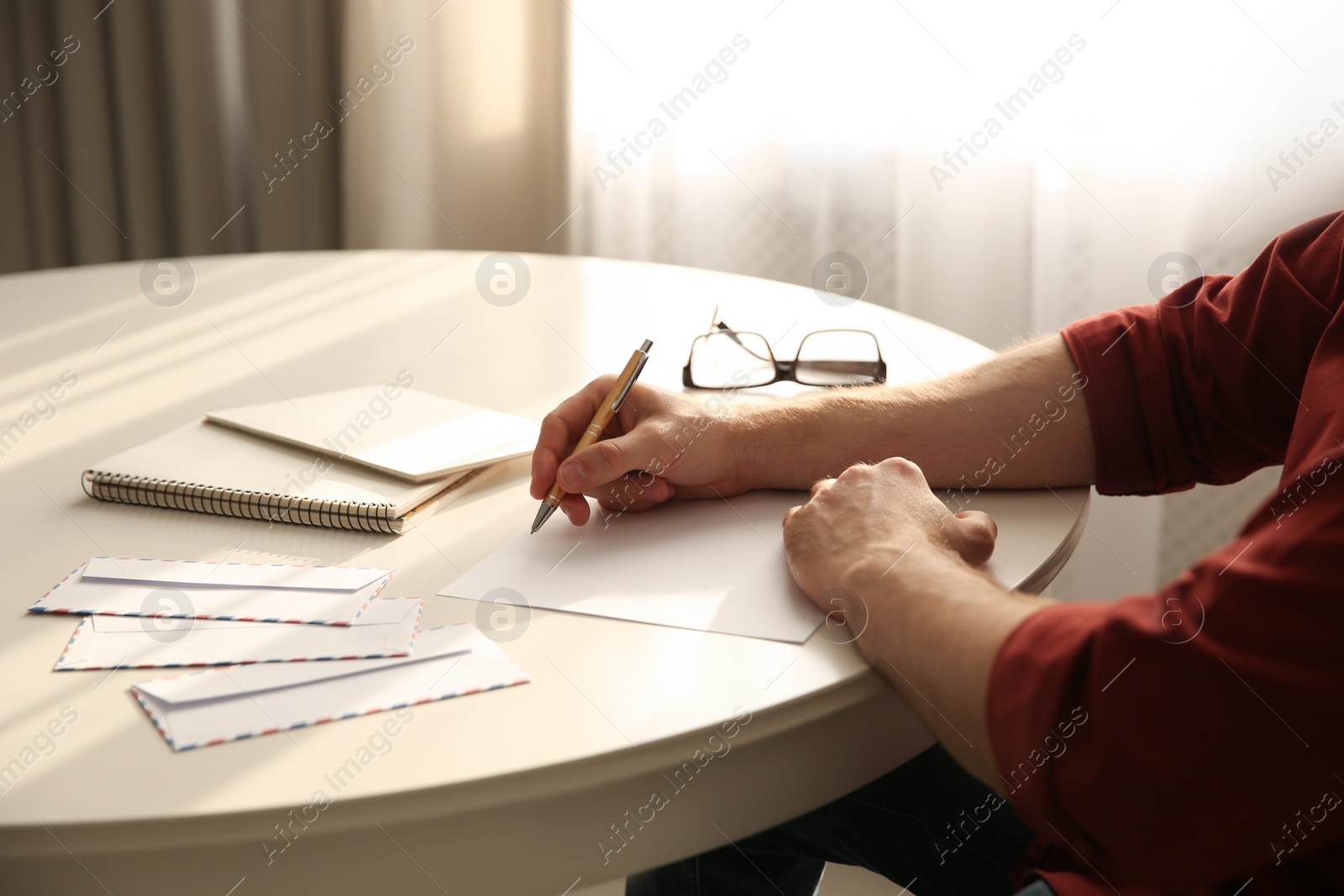 Photo of Man writing letter at white table in room, closeup