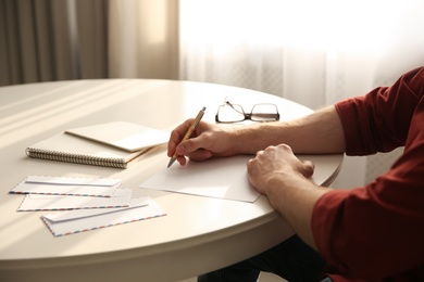 Man writing letter at white table in room, closeup