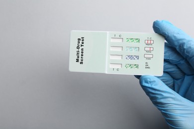 Doctor holding multi-drug screen test on light grey background, top view
