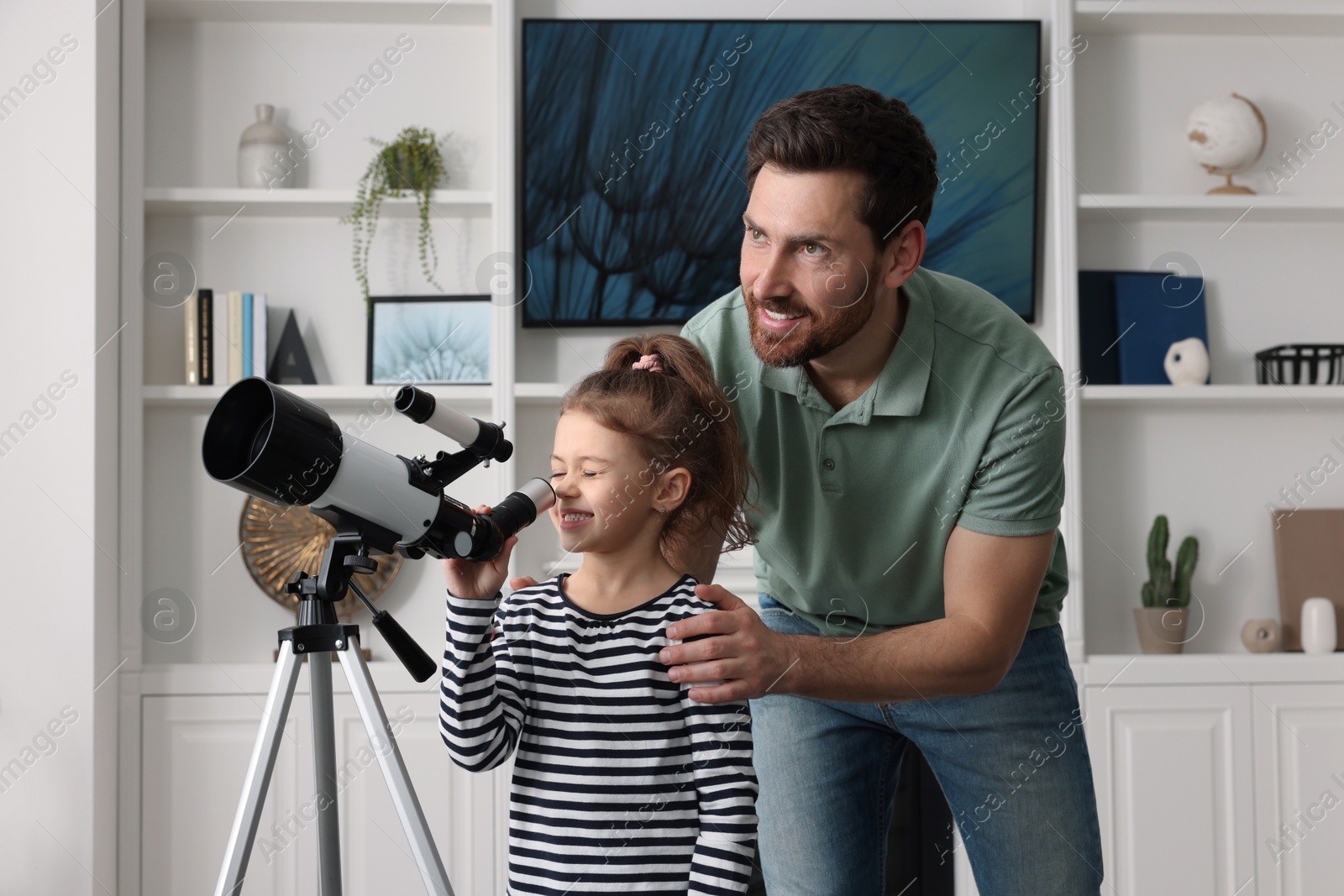 Photo of Little girl with his father looking at stars through telescope in room