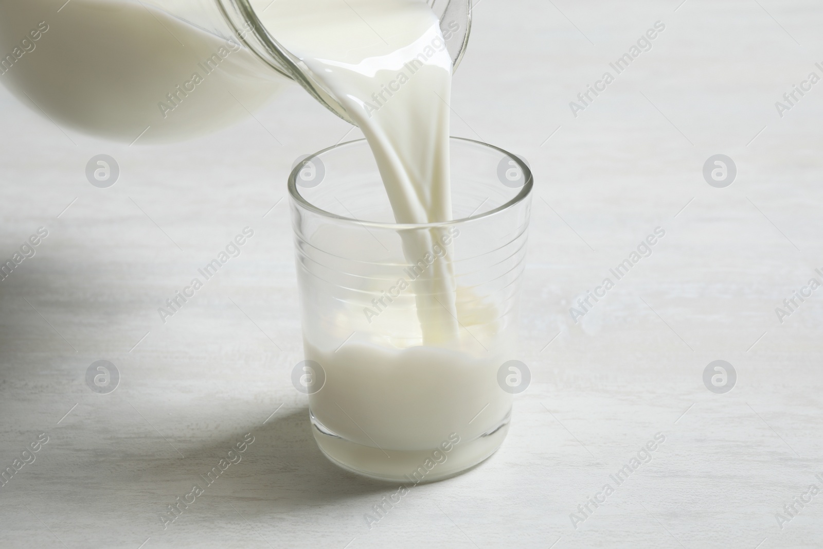 Photo of Pouring milk into glass on white table