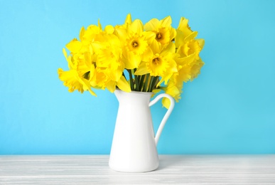 Photo of Bouquet of daffodils in jug on table against color background. Fresh spring flowers