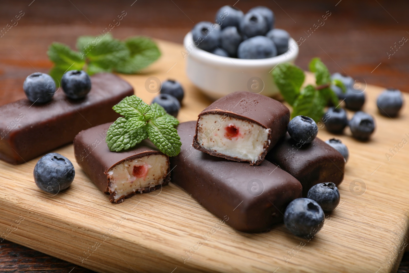 Photo of Delicious glazed curd snacks with blueberries on wooden table, closeup