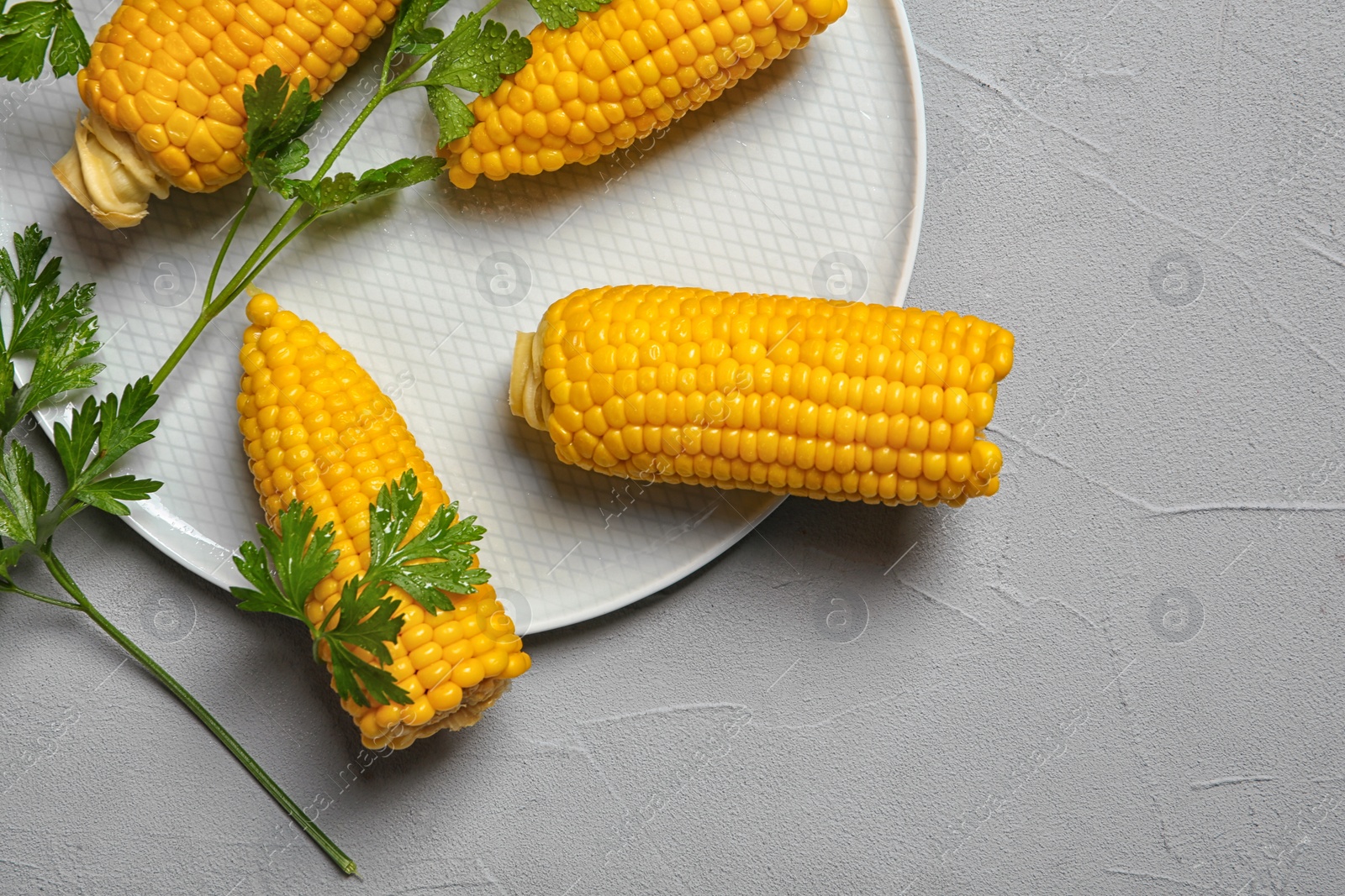 Photo of Plate with ripe corn cobs and parsley on grey background, top view. Space for text