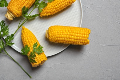 Plate with ripe corn cobs and parsley on grey background, top view. Space for text