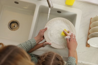 Mother and daughter washing plate above sink, top view
