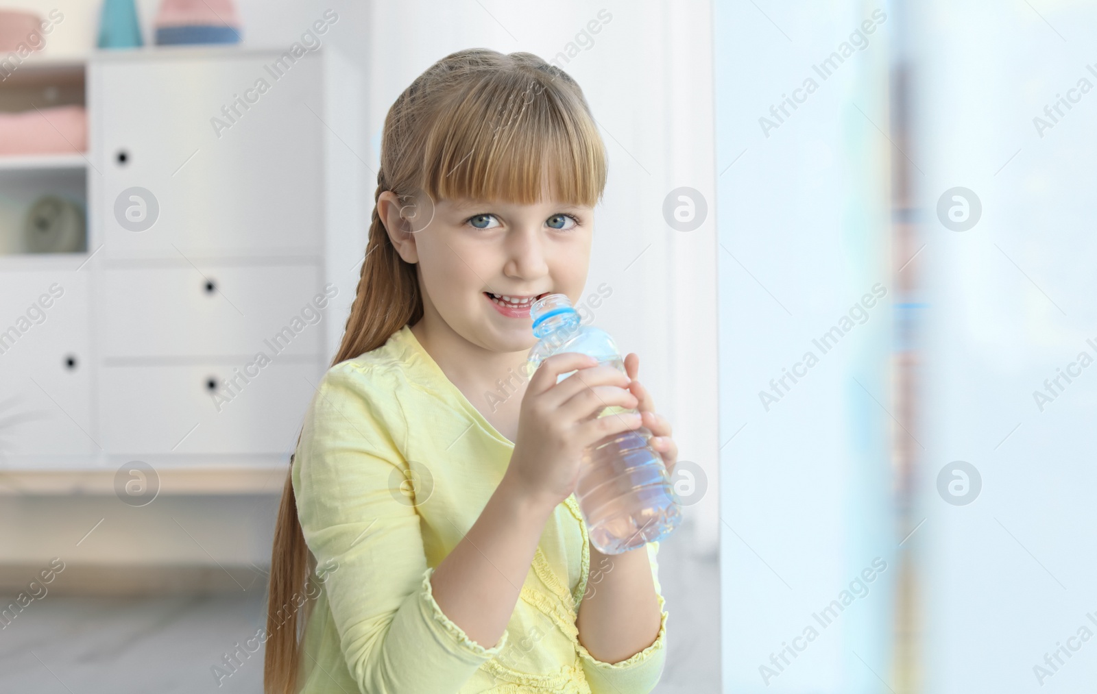 Photo of Cute little girl holding bottle with water indoors