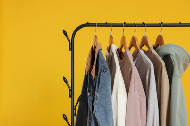 Photo of Rack with stylish clothes on wooden hangers against orange background, space for text