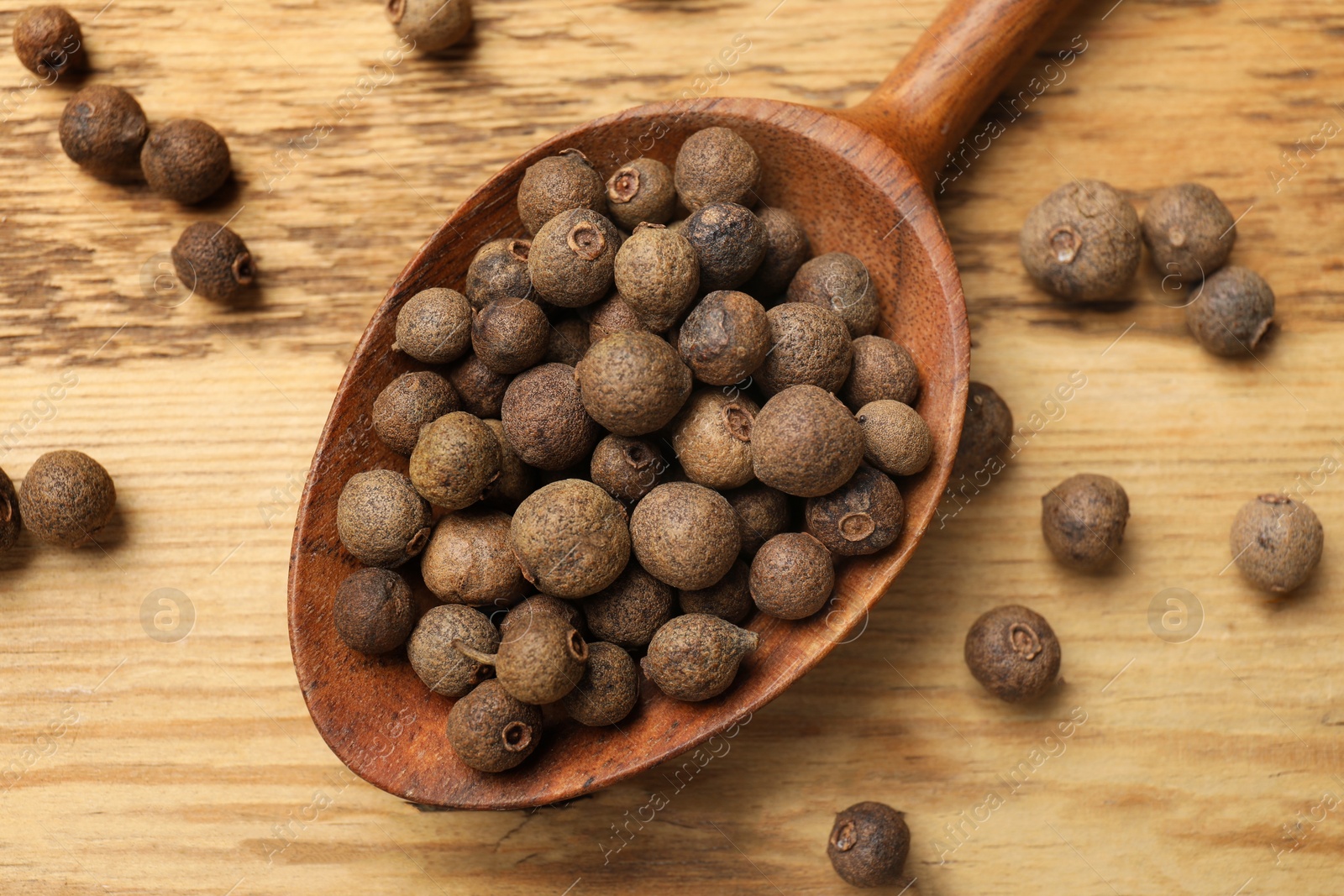 Photo of Dry allspice berries (Jamaica pepper) and spoon on wooden table, top view