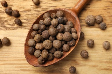 Dry allspice berries (Jamaica pepper) and spoon on wooden table, top view