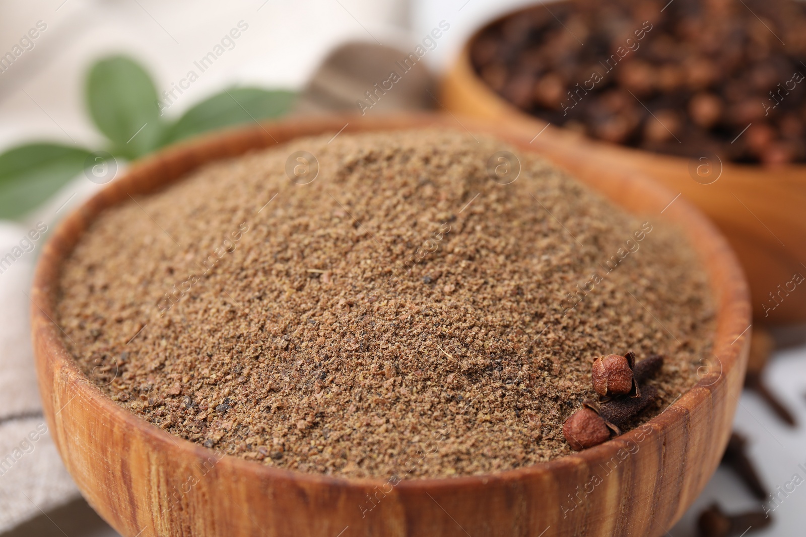 Photo of Aromatic clove powder and dried buds in bowl on table, closeup