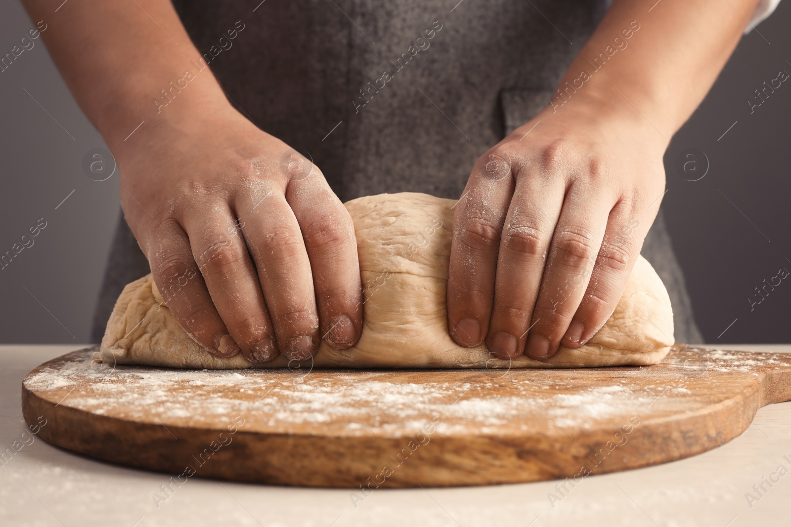 Photo of Man kneading dough at table near grey wall, closeup