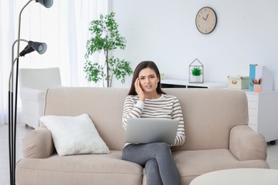 Photo of Young woman suffering from headache while sitting on sofa at home