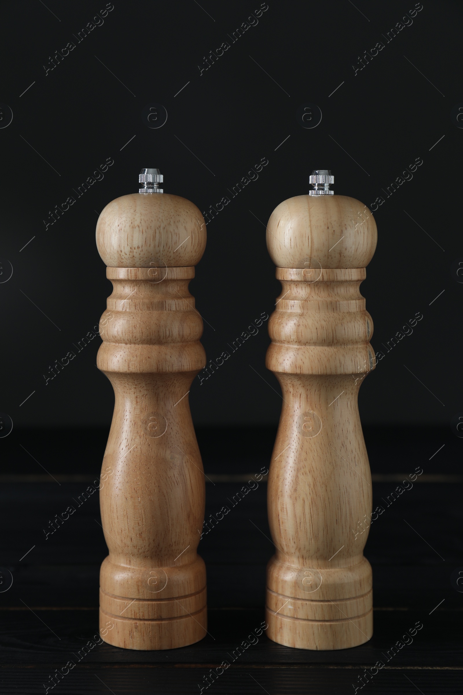 Photo of Salt and pepper shakers on black wooden table, closeup