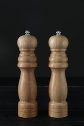 Photo of Salt and pepper shakers on black wooden table, closeup