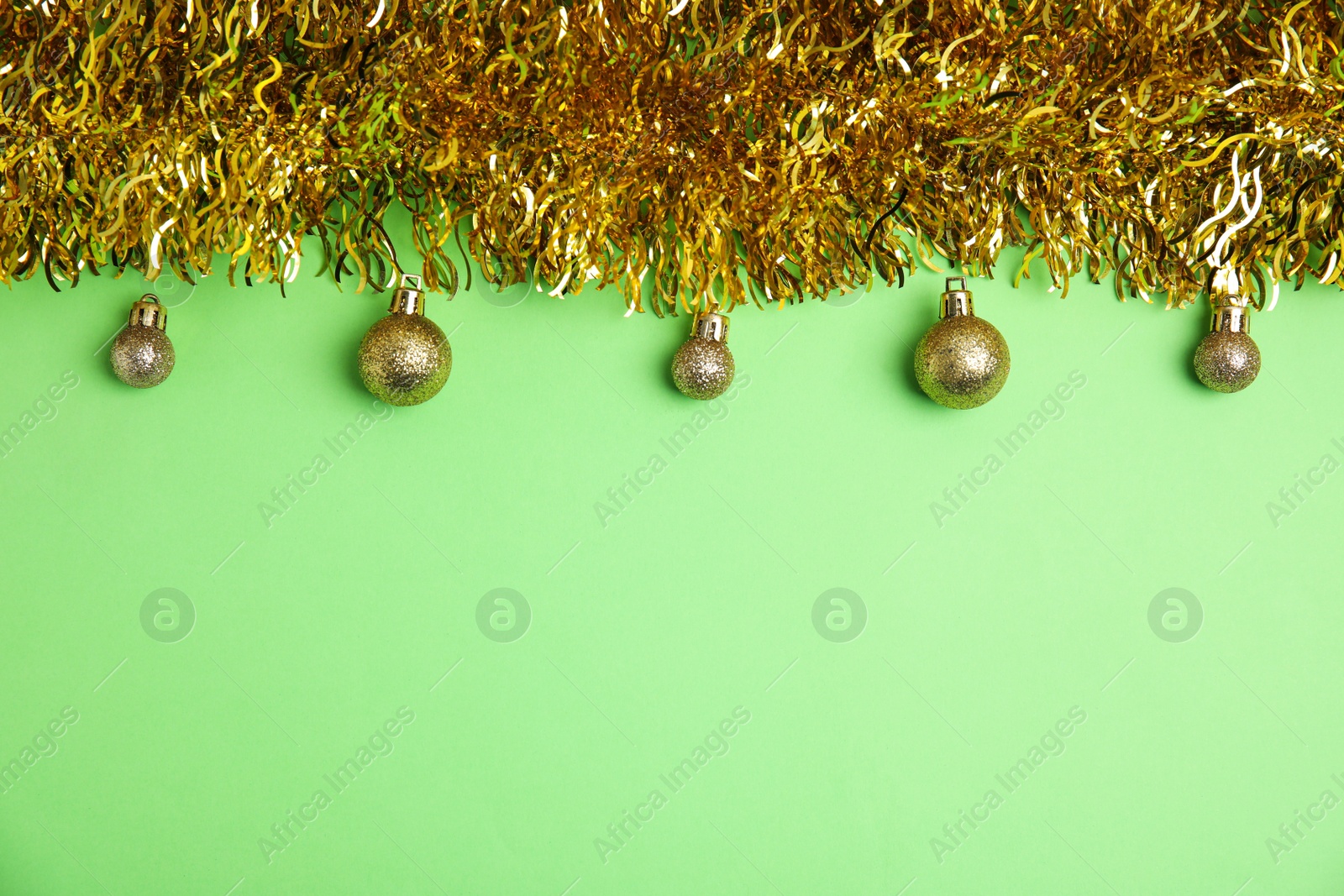 Photo of Golden tinsel and Christmas balls on green background, flat lay. Space for text