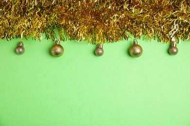 Golden tinsel and Christmas balls on green background, flat lay. Space for text