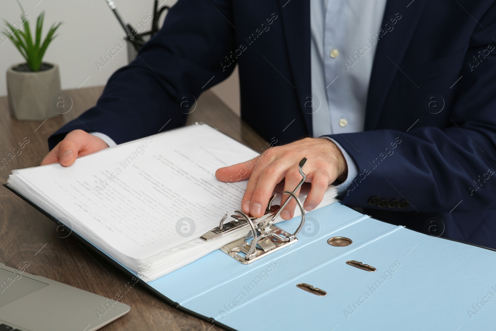 Photo of Businessman putting document into file folder at wooden table in office, closeup