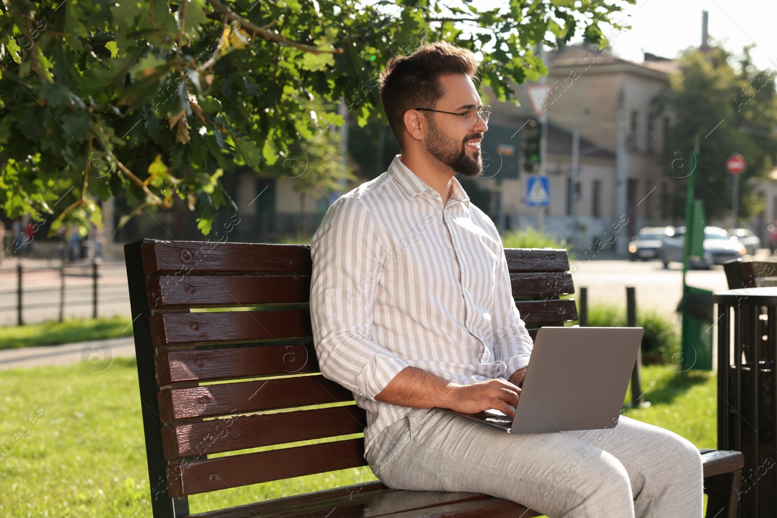 Photo of Young man using laptop on bench in park