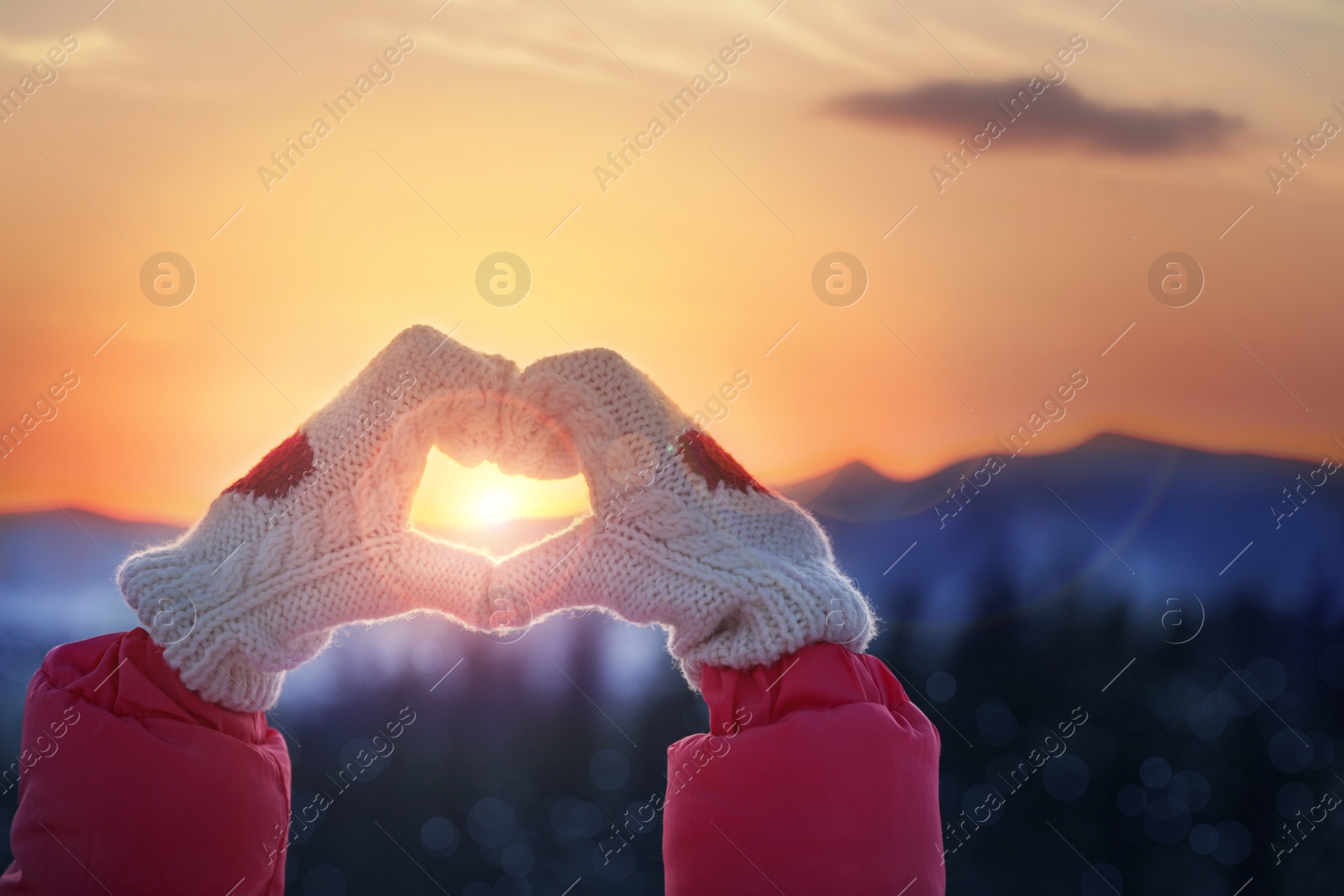 Image of Woman making heart with her hands in mountains at sunset, closeup. Winter vacation