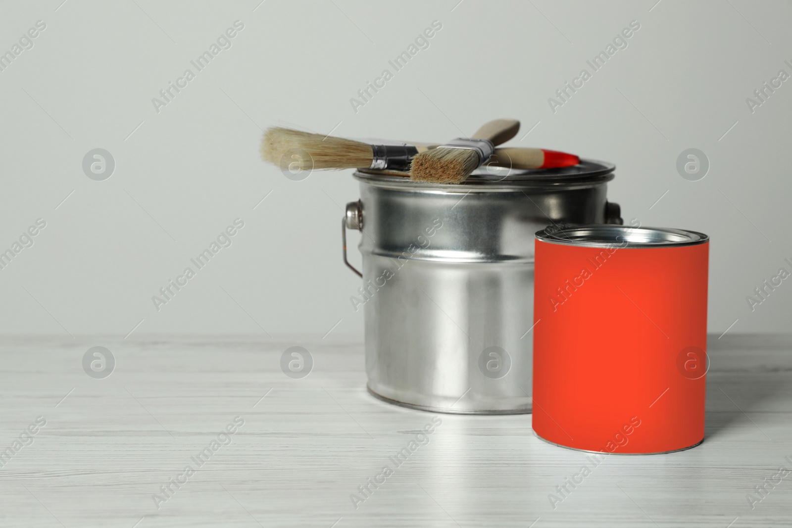 Photo of Can of orange paint, bucket and brushes on white wooden table. Space for text