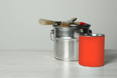 Photo of Can of orange paint, bucket and brushes on white wooden table. Space for text