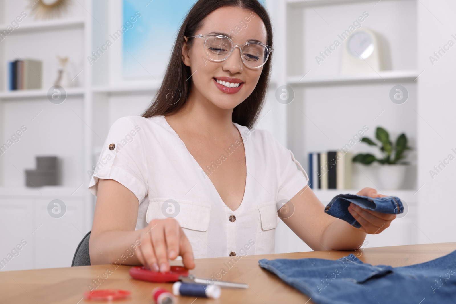 Photo of Happy woman holding cut hem and jeans at table indoors