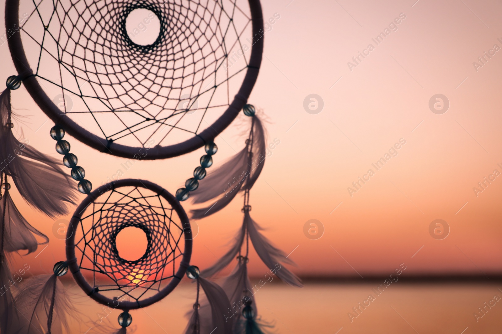 Photo of Beautiful handmade dream catcher near river at sunset. Space for text