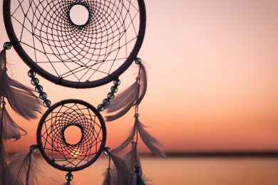 Photo of Beautiful handmade dream catcher near river at sunset. Space for text