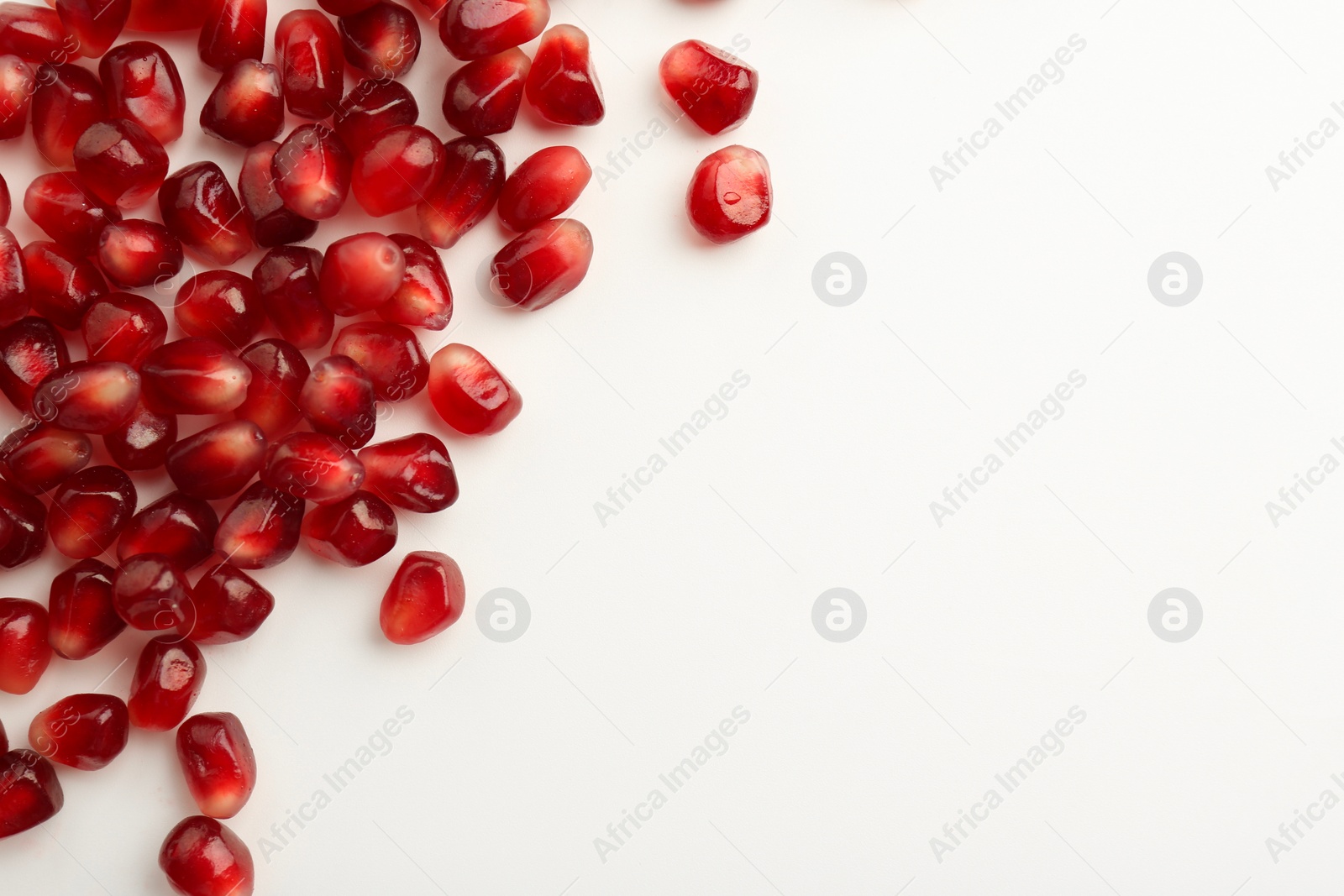 Photo of Many ripe juicy pomegranate grains on white background, flat lay. Space for text