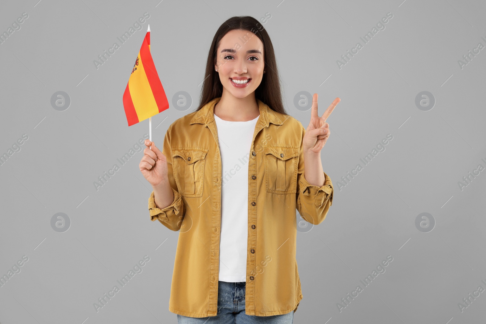 Photo of Young woman holding flag of Spain on light grey background