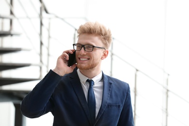 Portrait of handsome young man in elegant suit with glasses talking on mobile phone indoors