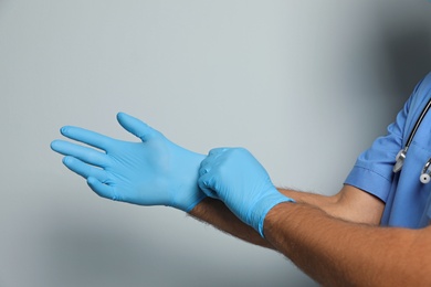 Doctor putting on medical gloves against light grey background, closeup