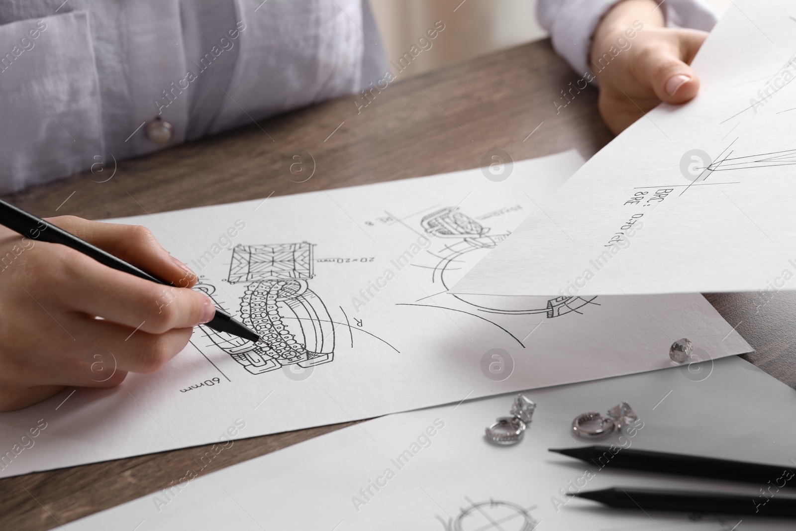 Photo of Jeweler drawing sketch of elegant earrings at wooden table, closeup