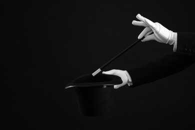 Magician showing magic trick with top hat on black background, closeup