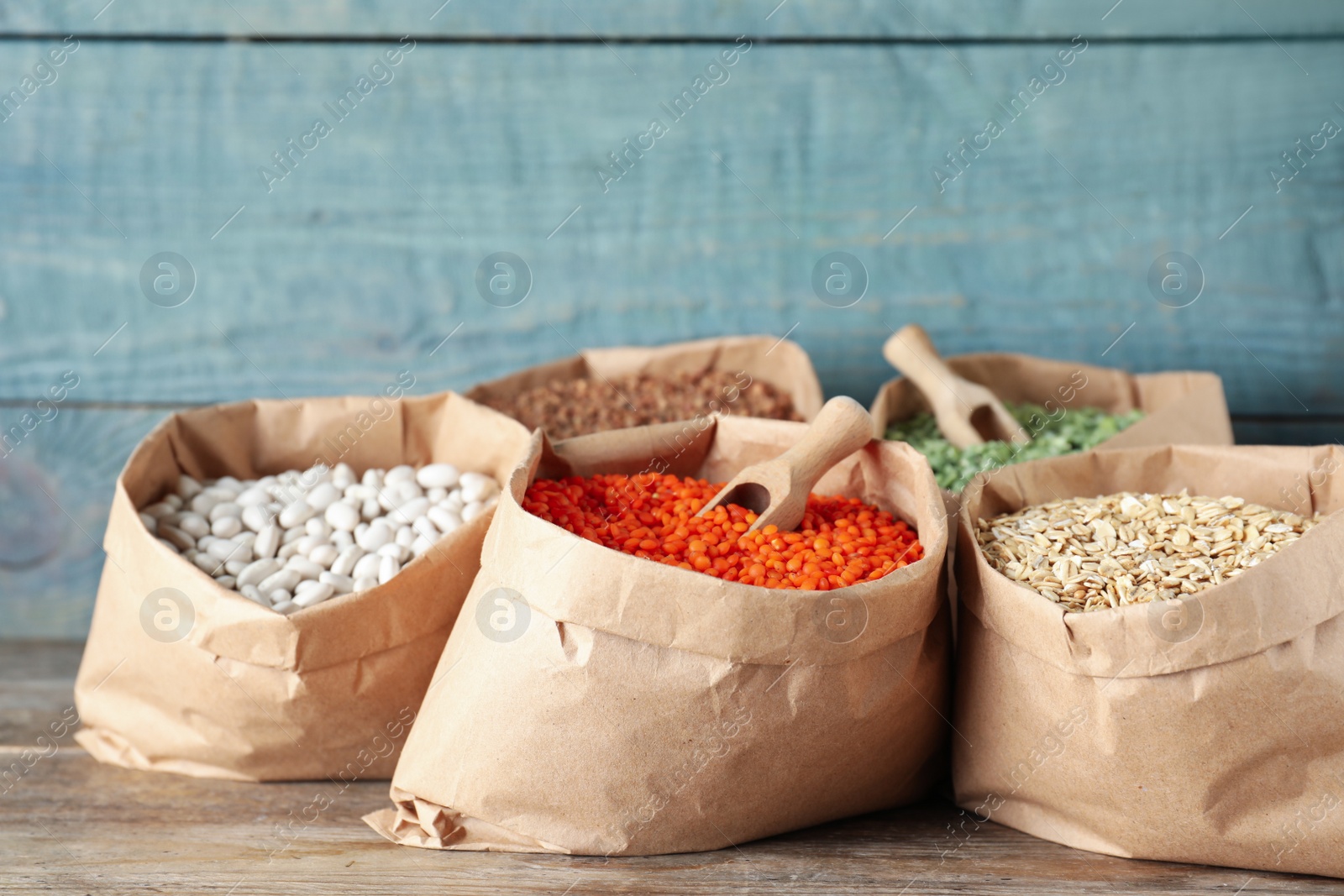 Photo of Different grains and cereals in paper bags on wooden table