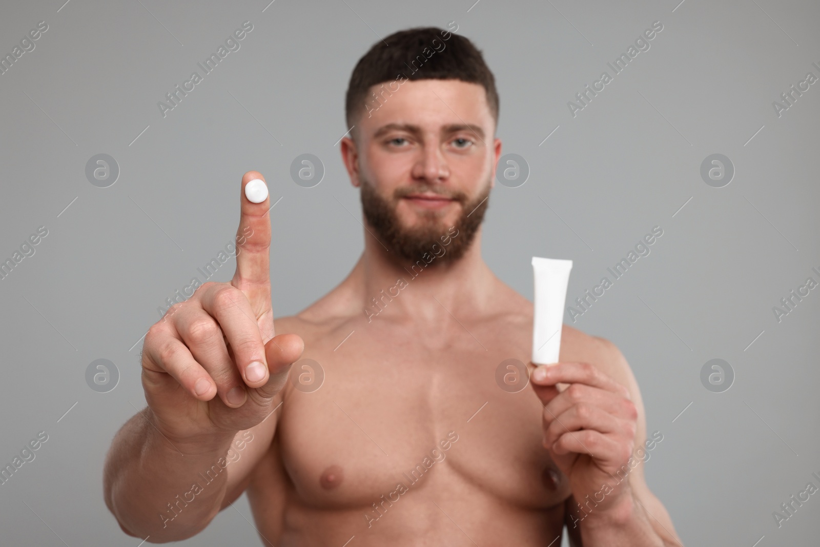 Photo of Handsome man with tube of body cream on light grey background, selective focus