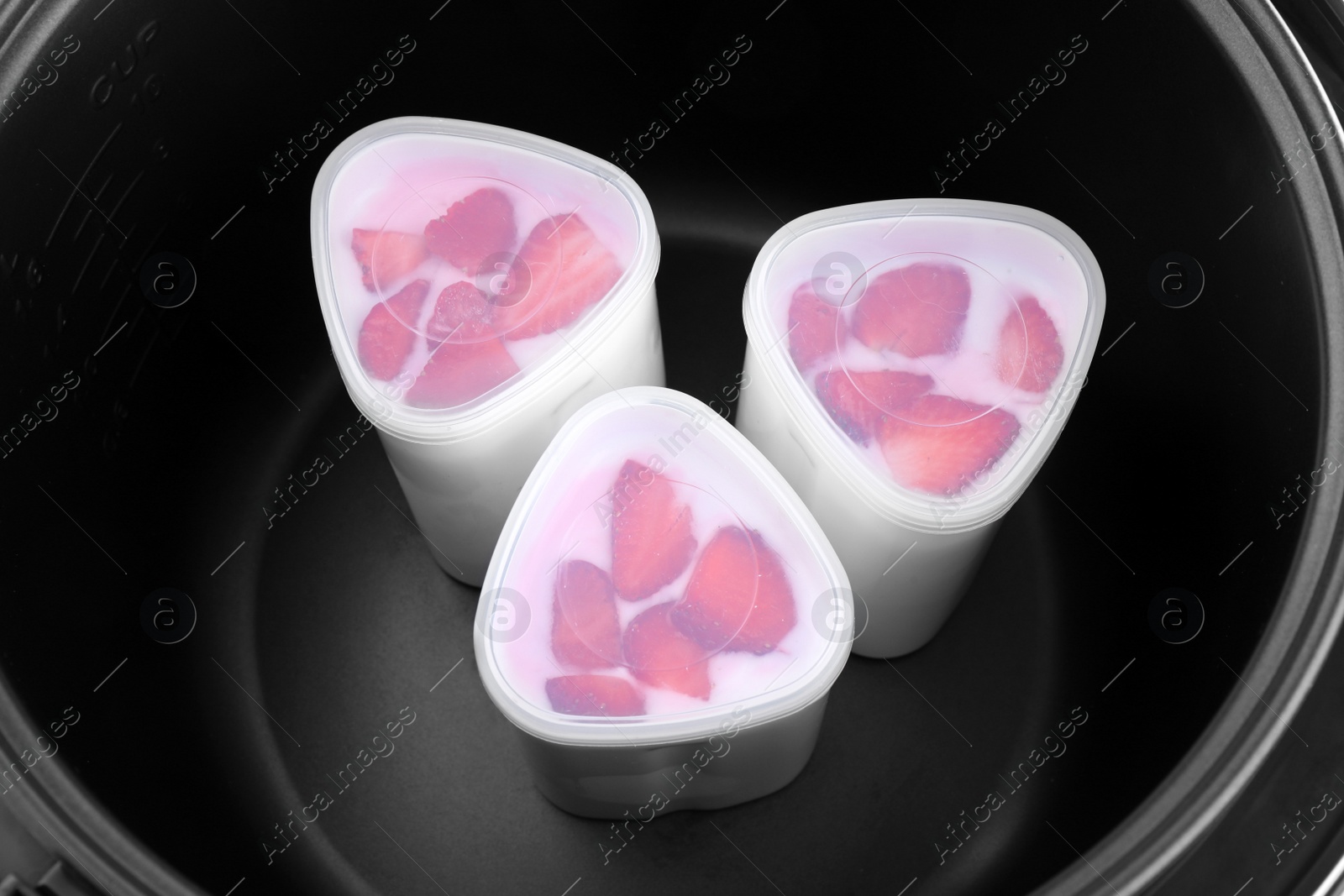 Photo of Cups of homemade strawberry yogurt in modern multi cooker, closeup view